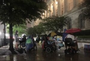 Activists sit in the rain outside the Capitol to protest cuts to Medicaid