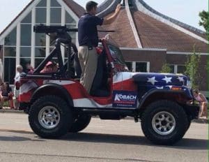 Kansas Republican Secretary of State Kris Kobach, also a candidate for governor, rides in a parade with a replica machine gun on his vehicle