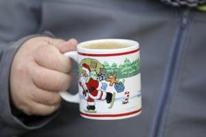A man holds a Christmas-themed coffee mug.