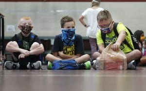 Kids sit crosslegged wearing masks in school