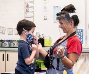 Kindergarten teacher helps child with mask