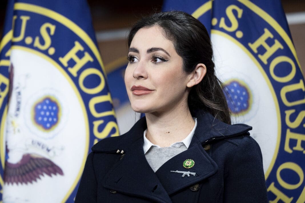 U.S. Representative Anna Paulina Luna (R-FL) speaking at a Congressional Hispanic Conference press conference at the U.S. Capitol. On the lapel of her coat below her Congressional pin is a pin shaped like an assault rifle.