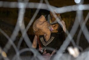 A migrant couple struggles while carrying their baby as they approach a gate in the border fence after crossing from Ciudad Juarez, Mexico into El Paso, Texas, in the early hours of Thursday, May 11, 2023.