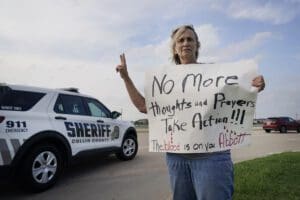 Mary Ann Foley holds a protest sign outside a prayer vigil following a mass shooting the day before, Sunday, May 7, 2023, in Allen, Texas.